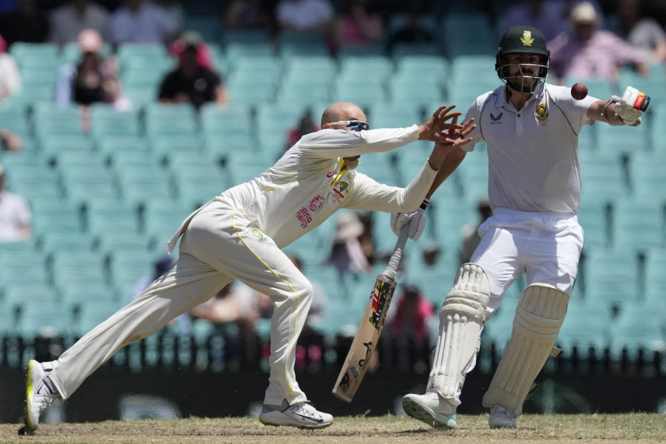 Australia's Nathan Lyon, left, reaches to catch out South Africa's Kagiso Rabada off his own bowling as South Africa's Anrich Nortje, right looks on during the fifth day of their cricket test match at the Sydney Cricket Ground in Sydney, Sunday, Jan. 8, 2023. (AP Photo/Rick Rycroft)