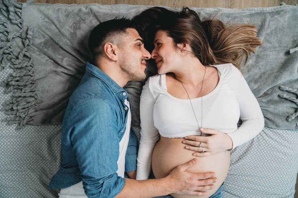 Millennial pregnant couple lying down on bed together. High angle view.