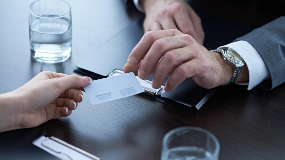 Hand of woman giving business card to businessman.