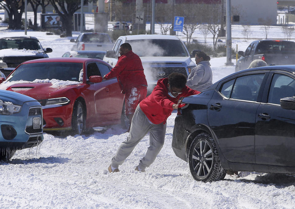 People push a car free after spinning out in the snow Monday, Feb. 15, 2021 in Waco, Texas. A winter storm that brought snow, ice and plunging temperatures across the southern Plains and caused a power emergency in Texas stretched its frigid fingers down to the Gulf Coast. (Jerry Larson/Waco Tribune-Herald via AP)