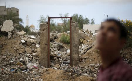 A Palestinian teen stands next to the frame of a destroyed house doorway, on which British street artist Banksy painted an image of a goddess holding her head in her hand, after the door with the painted image was sold in the northern Gaza Strip April 1, 2015. REUTERS/Mohammed Salem