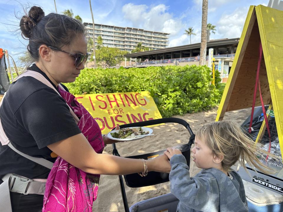 Jordan Ruidas feeds her son at the Fishing for Housing protest camp on Kaanapali Beach in Lahaina, Hawaii on Wednesday, Nov.14, 2023. A group of Lahaina wildfire survivors is vowing to camp on a popular resort beach until the mayor uses his emergency powers to shut down unpermitted vacation rentals and make the properties available for residents in desperate need of housing. (AP Photo/Audrey McAvoy)