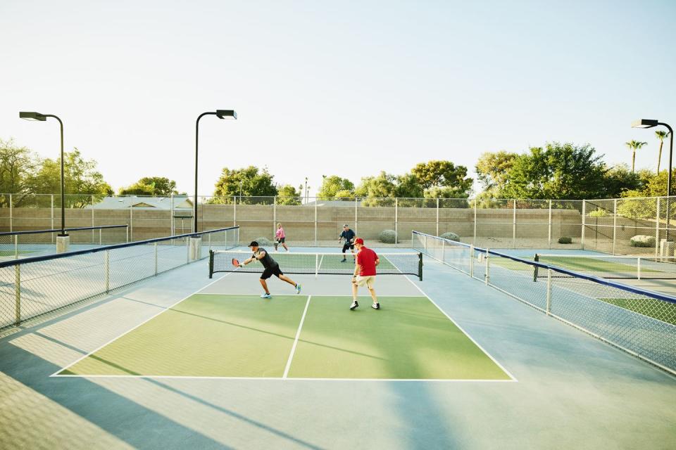 extreme wide shot of senior friends playing doubles pickleball on sunny summer evening