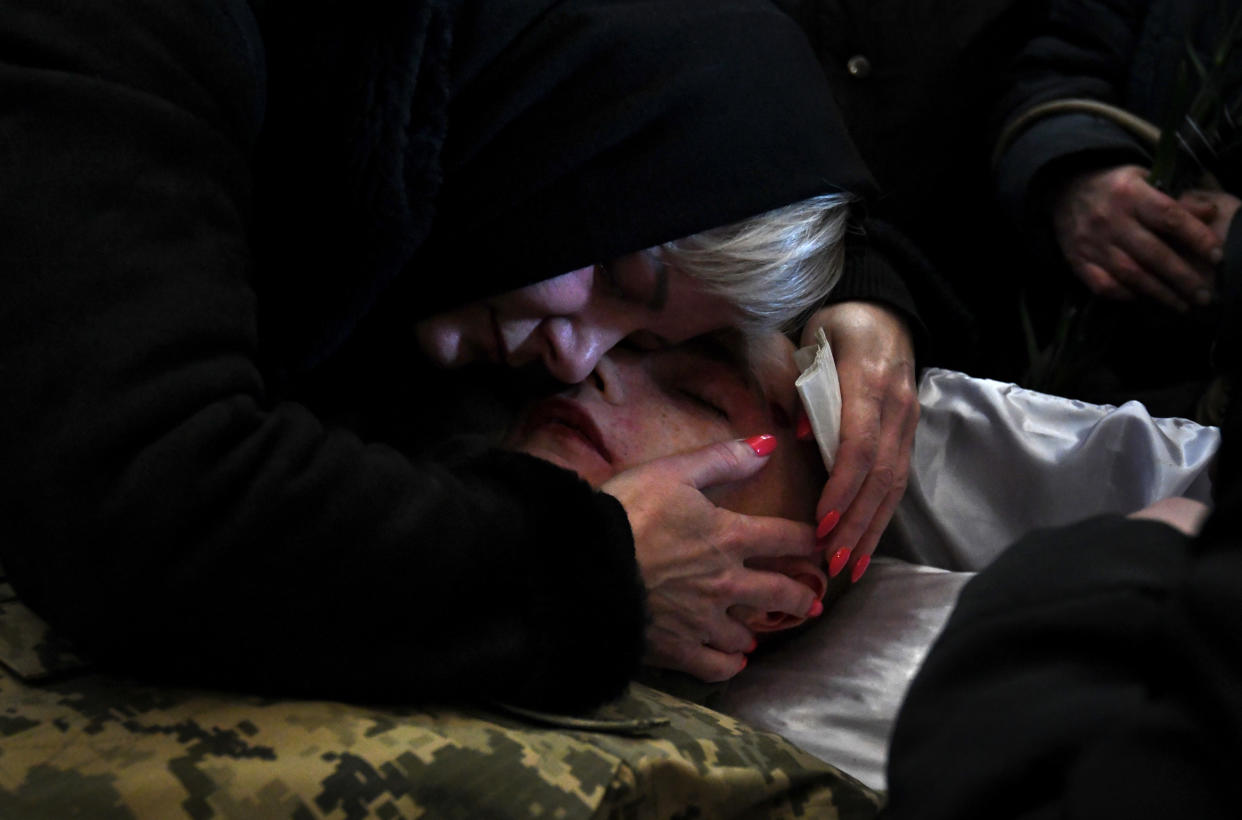 A mother embraces the body of her son, who is lying in a casket.