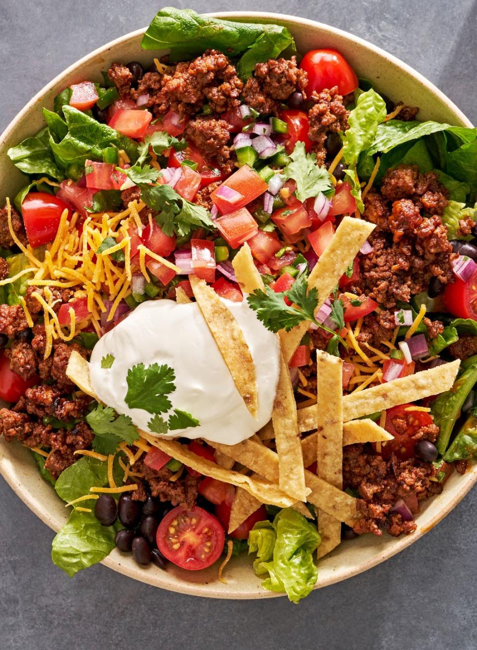 romaine salad topped with ground beef, sour cream, black beans, diced tomatoes, shredded cheese, diced red onion, fried tortilla strips, and cilantro