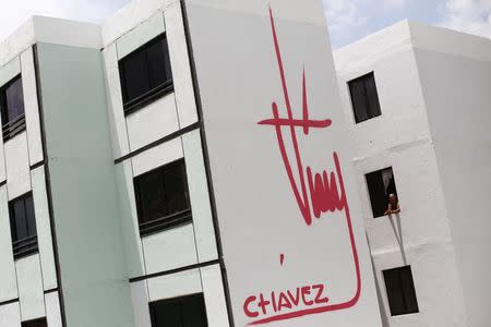 A woman stands at a window of a building bearing a design of the signature of late Venezuelan President Hugo Chavez in Ciudad Caribia outside Caracas in this September 19, 2013 file photo. REUTERS/Jorge Silva/Files