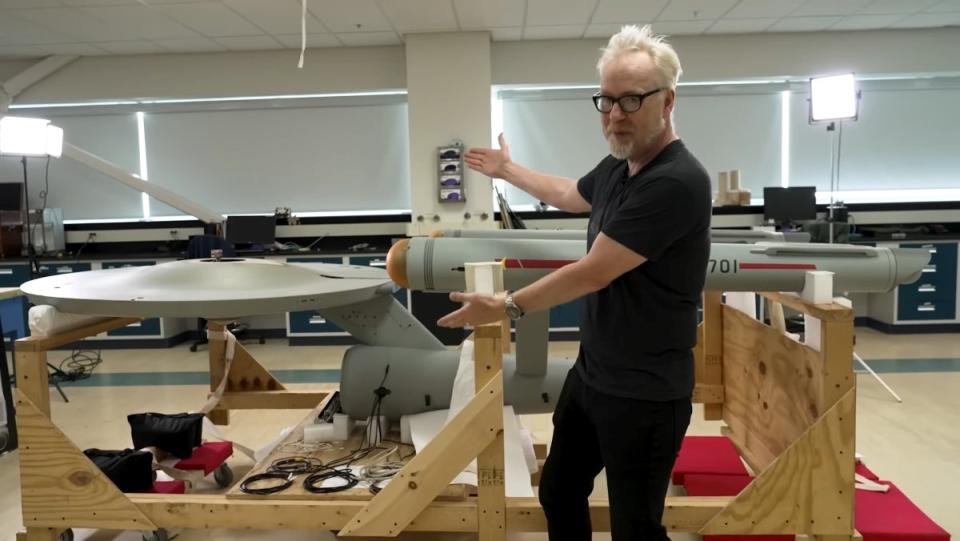 Adam Savage gestures to the model of the U.S.S. Enterprise from Star Trek at the Smithsonian Air and Space Museum