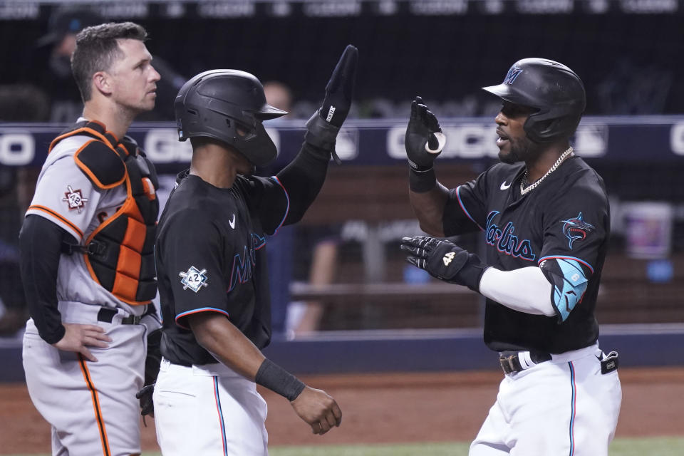 Miami Marlins' Magneuris Sierra, center, congratulates Starling Marte (6) after Marte hit a three-run home run in the eighth inning of a baseball game against the San Francisco Giants, Friday, April 16, 2021, in Miami. To the left is Giants catcher Buster Posey. (AP Photo/Marta Lavandier)