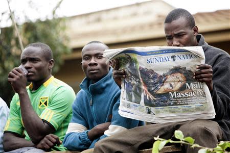 A man reads a daily newspaper with other onlookers at the edge of a security perimeter put into place near the Westgate shopping centre where gunmen are holding hostages, in Nairobi September 22, 2013. REUTERS/Siegfried Modola