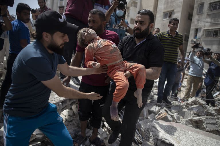 Los hombres llevan a un niño muerto sacado de los escombros de un edificio residencial destruido en la ciudad de Gaza luego de los ataques aéreos israelíes el 16 de mayo, que derribaron tres edificios y mataron al menos a dos docenas de personas, según los médicos. 
