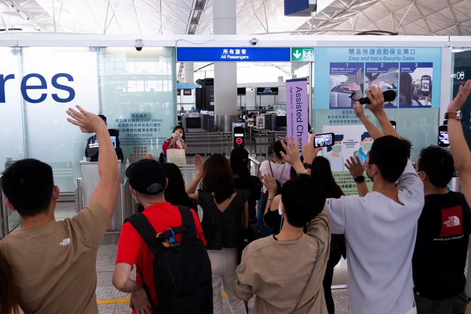 A woman (back C) takes photos of her friends waving goodbye to her before entering the departures hall for her flight to Britain at Hong Kong's International Airport on July 18, 2021, the day before a deadline by the British government to allow Hong Kongers the right to visit the UK if not eligible to enter under an existing immigration route.  / AFP / Bertha WANG