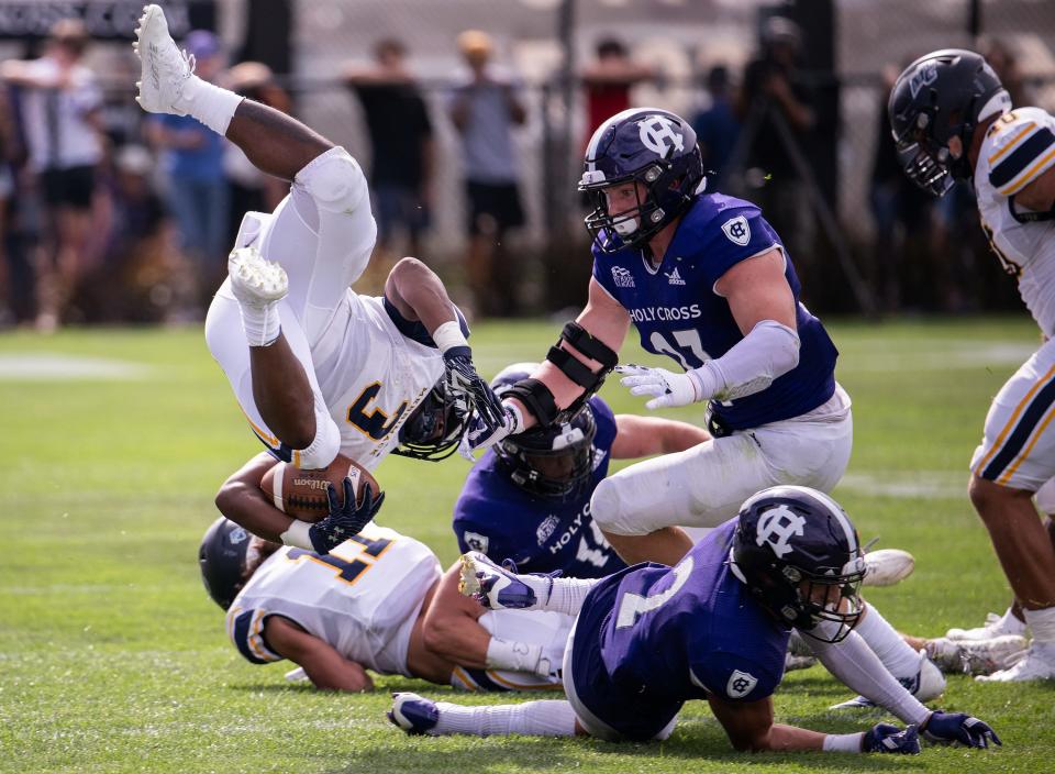 Merrimack's Donte Williams is flipped in the air and brought down by Holy Cross's Matt Duchemin (2) and Jacob Dobbs (27) Saturday at Fitton Field.