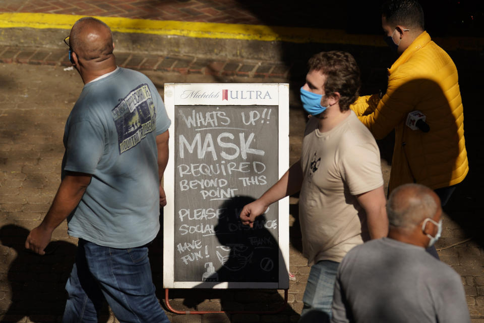 Visitors wearing face masks walk past a sign requiring masks at a restaurant along the River Walk, Wednesday, March 3, 2021, in San Antonio. Gov. Greg Abbott says Texas is lifting a mask mandate and lifting business capacity limits next week. (AP Photo/Eric Gay)