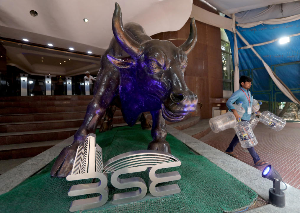 FILE PHOTO: A man carries empty water bottles past a bronze replica of the Charging Bull of Wall Street, inside the premises of the Bombay Stock Exchange (BSE) in Mumbai, February 1, 2023. REUTERS/Niharika Kulkarni/File Photo