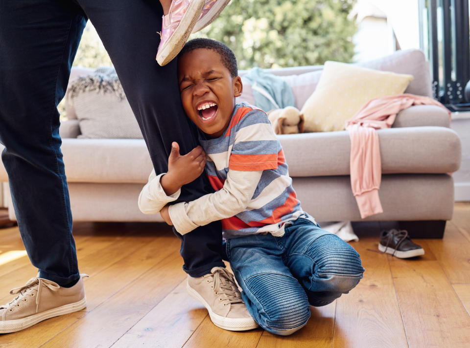 Child holding knee in pain after tripping, adult reaching out to soothe, indoors with couch in background