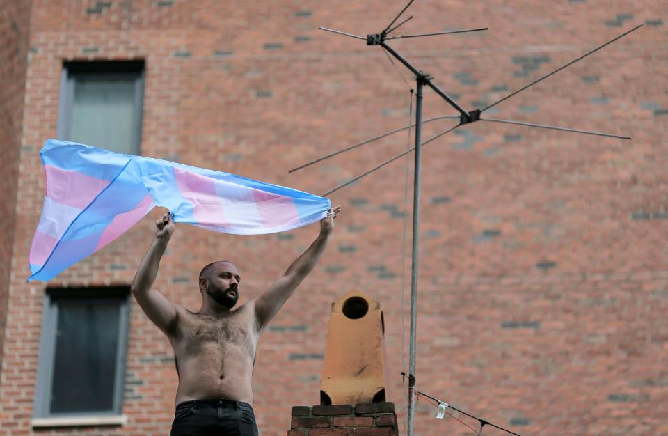 A man waves a transgender pride flag as the Queer Liberation March passes below in New York, Sunday, June 30, 2019.