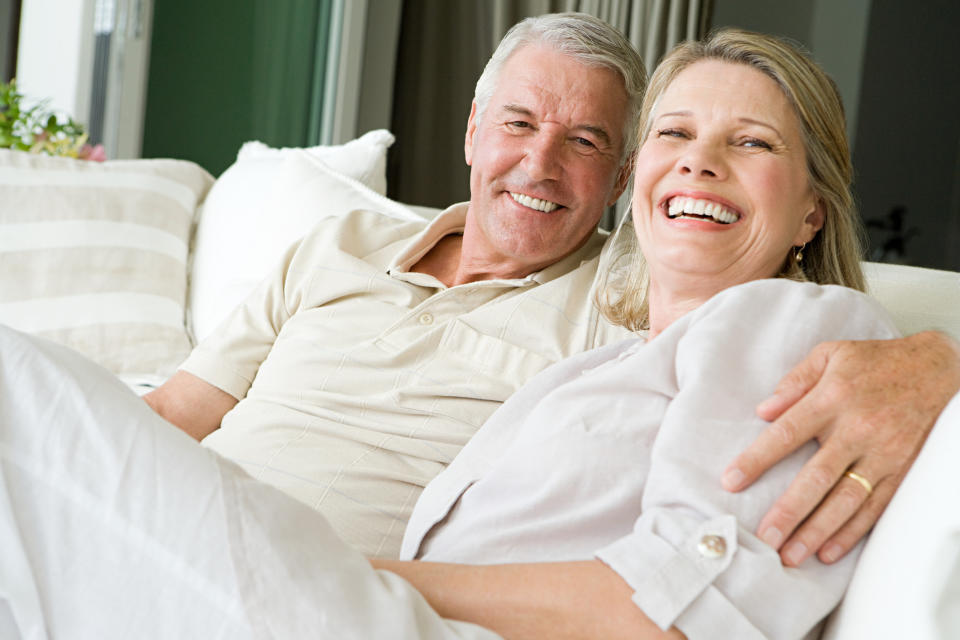 Older couple smiling, sitting on a sofa.