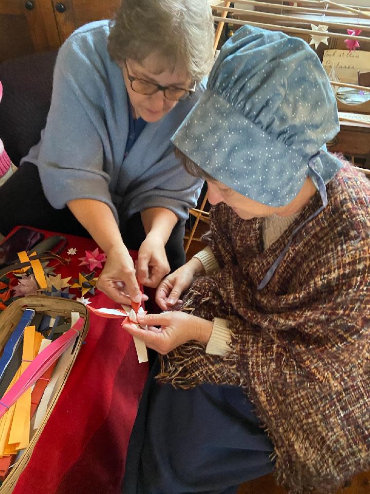 Kathy Scott works with Diane Fortner as she learns to fold a Moravian star -- ornaments that made their way to our country from German. The activity was part of "Celebrating Christmas" with a focus on Germany.