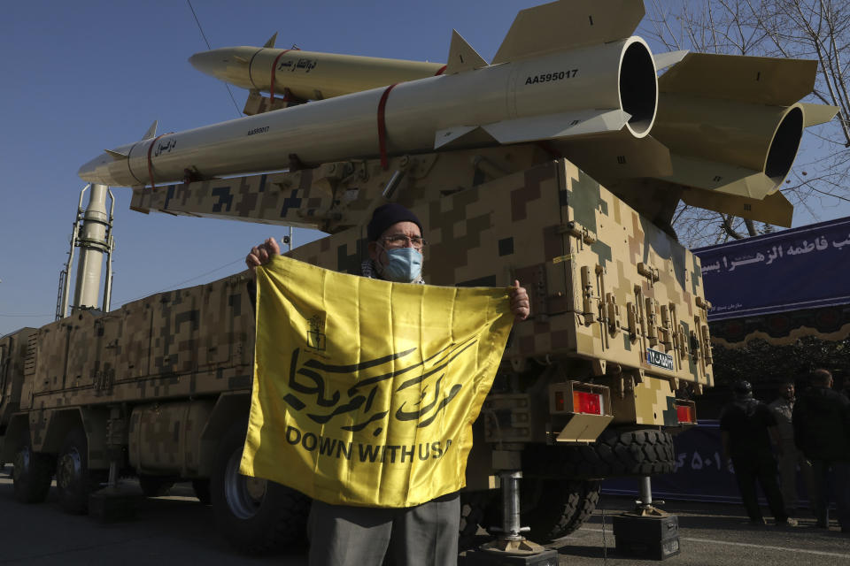 A man holds an anti-U.S. banner in front of Zolfaghar, top, Dezful, bottom, and Qiam, background left, missiles displayed in a missile capabilities exhibition by the paramilitary Revolutionary Guard a day prior to second anniversary of Iran's missile strike on U.S. bases in Iraq in Tehran, Iran, Friday, Jan. 7, 2022. Iran put three ballistic missiles on display at an outdoor prayer esplanade in central Tehran on Friday, as talks in Vienna aimed at reviving Tehran’s nuclear deal with world powers flounder.(AP Photo/Vahid Salemi)