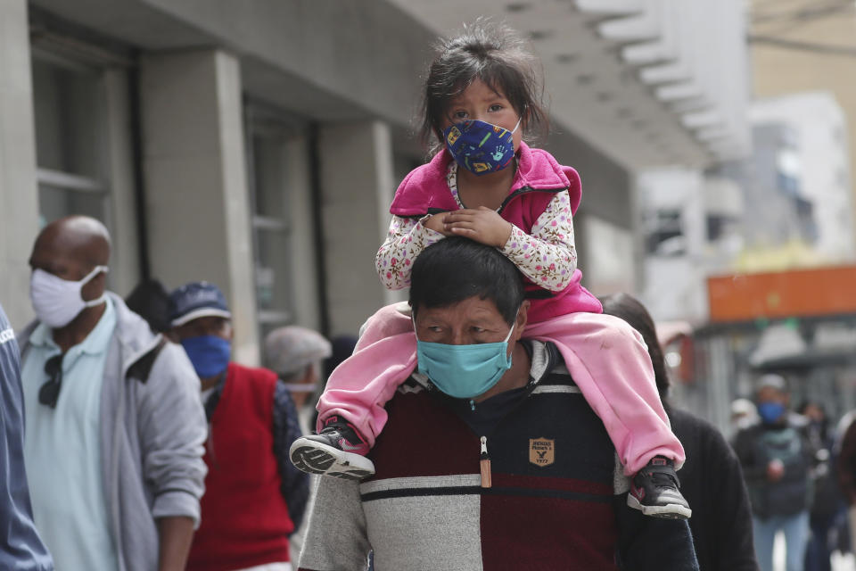A child, wearing a protective face mask as a mandatory measure to help curb the spread of the new coronavirus, rides piggyback through a crowded downtown area in Quito, Ecuador, Wednesday, June 10, 2020. The city is returning to a new normality after relaxing a rigorous quarantine but amid a certain fear that COVID-19 infections may rise. (AP Photo/Dolores Ochoa)