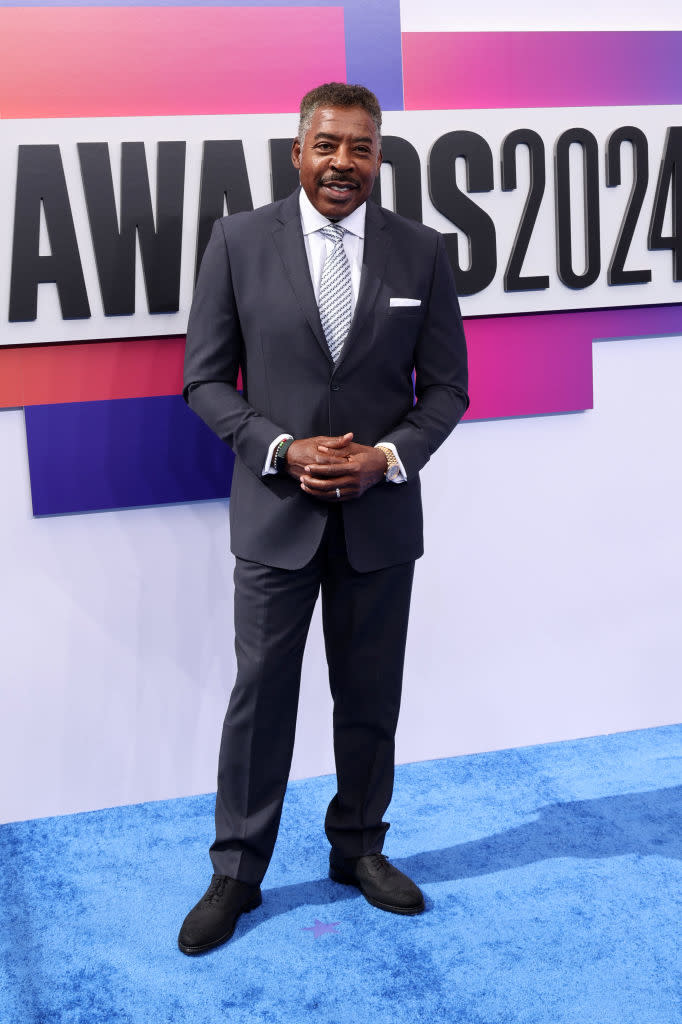 Ernie Hudson in a dark suit and striped tie, standing on a blue carpet at the 2024 Awards