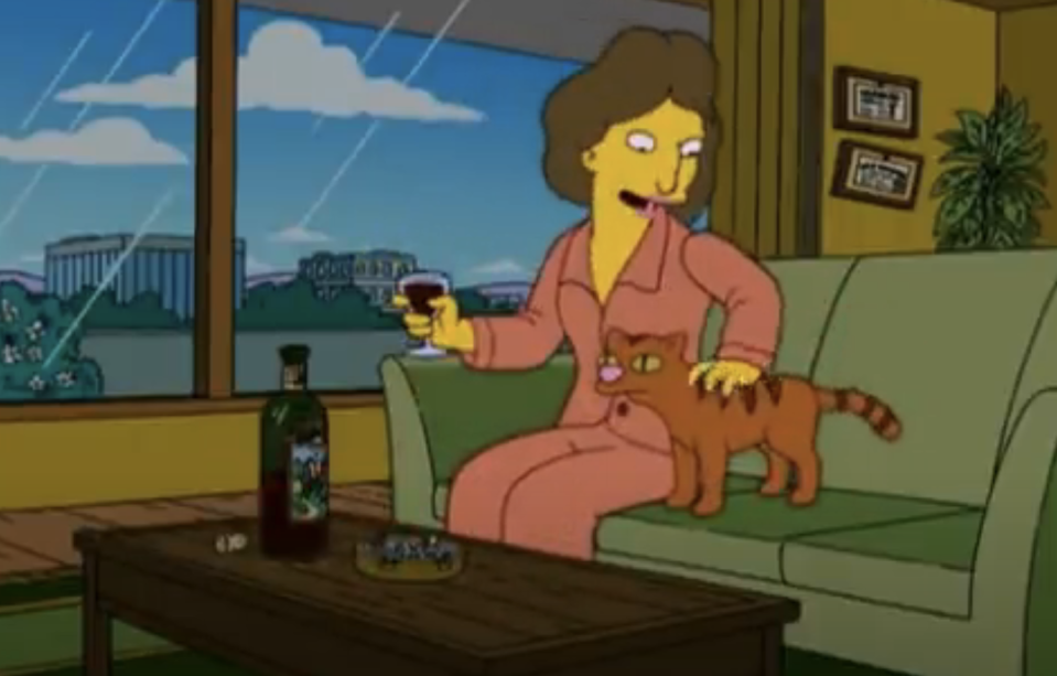 Marge Simpson is sitting on a couch, holding a glass of wine, and petting the cat, Snowball II. A bottle of wine and an ashtray are on the coffee table
