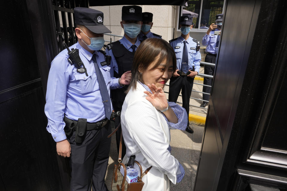 Teresa Xu waves as she walks near Chinese policemen at the entrance to the Beijing No.3 Intermediate People's Court before her appeal hearing in Beijing, Tuesday, May 9, 2023. The unmarried Chinese woman on Tuesday began her final appeal of a hospital's denial of access to freeze her eggs five years ago in a landmark case of female reproductive rights in the country. (AP Photo/Ng Han Guan)
