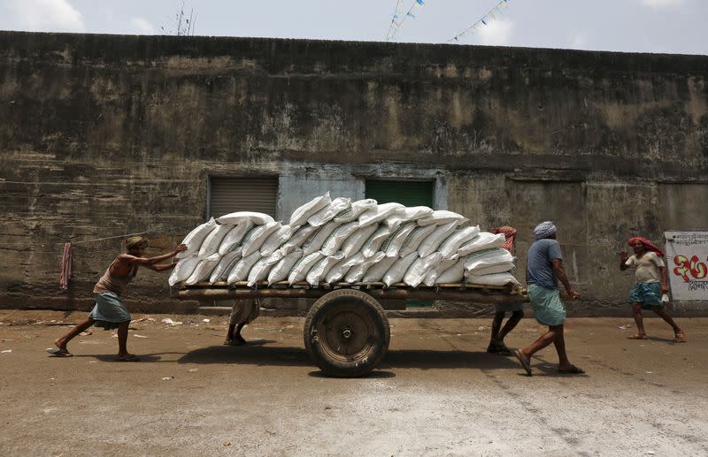 Labourers push a handcart loaded with sacks of sugar at a wholesale market in Kolkata