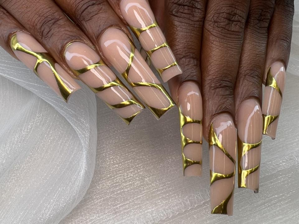 Long acrylic coffin nails set with abstract design in gold color, gold chrome design on long nails