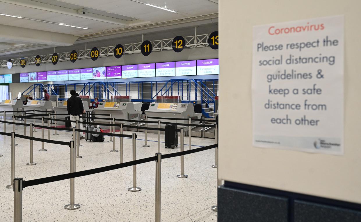 Passengers wearing PPE (personal protective equipment), including a face mask as a precautionary measure against COVID-19, observe social distancing measures as they wait at almost-empty check-in desks in the departure hall at Terminal 1 of Manchester Airport in Manchester, northern England on May 11, 2020, where they have begun a trial of body temperature screening during the COVID-19 pandemic. - Prime Minister Boris Johnson has announced plans to quarantine people arriving in Britain by air for 14 days to prevent new COVID-19 infections from abroad, under a phased lockdown easing that seeks to avoid a second spike. (Photo by Oli SCARFF / AFP) (Photo by OLI SCARFF/AFP via Getty Images)