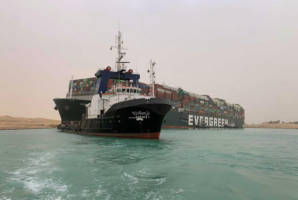 In this photo released by the Suez Canal Authority, a boat navigates in front of a massive cargo ship, named the Ever Green, rear, sits grounded Wednesday, March 24, 2021, after it turned sideways in Egypt’s Suez Canal, blocking traffic in a crucial East-West waterway for global shipping. An Egyptian official warned Wednesday it could take at least two days to clear the ship. (Suez Canal Authority via AP)