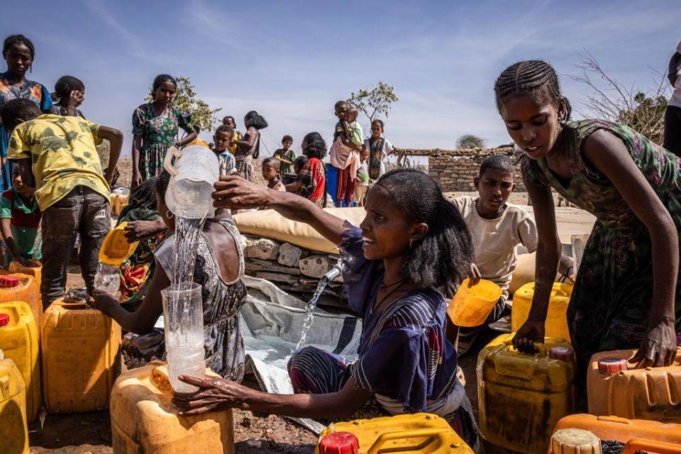 A woman pours water into a plastic bottle and fills larger yellow cans with water