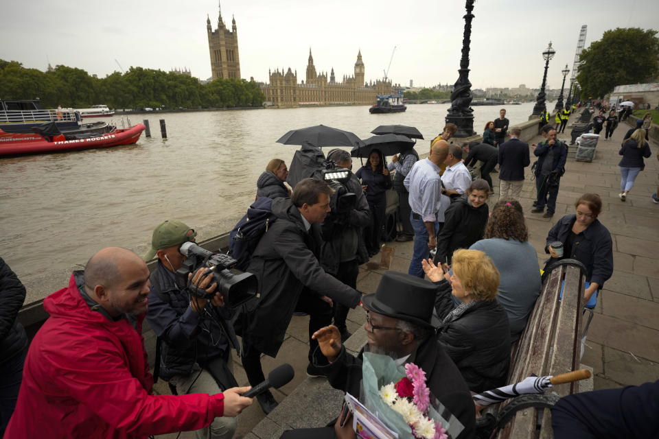 People are interviewed by TV reporters as they wait opposite the Palace of Westminster to be first in line bidding farewell to Queen Elizabeth II in London, Tuesday, Sept. 13, 2022. Queen Elizabeth II, Britain's longest reigning monarch, will be lying in state at Westminster Palace from Wednesday. ( (AP Photo/Markus Schreiber)