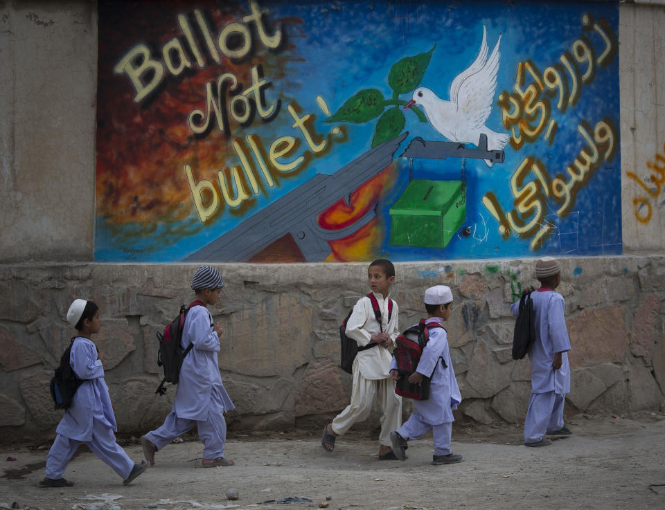 In this Wednesday, March 12, 2014 photo, school children pass by a graffiti reading, "ballot not bullet" on their way back home on the outskirts of Kandahar, southern Afghanistan. Warlords with a violent past have played a role in influencing Afghan politics since a U.S.-led coalition helped oust the Taliban in 2001. But they are emerging to play an overt political role in next month’s presidential elections as President Hamid Karzai leaves the scene. (AP Photo/Anja Niedringhaus)