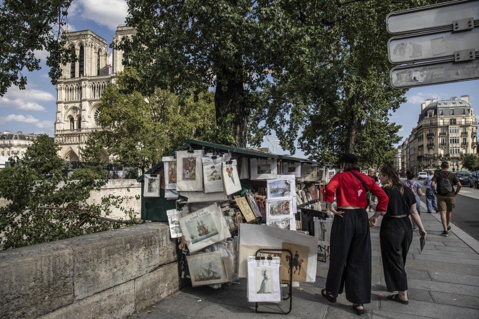 Women walk past bookseller booth, called "bouquiniste" along the Seine Riverbank in Paris, Tuesday, Aug. 22, 2023. The host city of Paris vowed to deliver an extraordinary grand opening on July 26, 2024, as the ceremony is expected to draw about 600,000 spectators to the Parisian quayside. Citing security measures, the Paris police prefecture ordered on July 25 the removal of 570 stationary boxes out of which booksellers have operated for decades on the quays of the Seine river. (AP Photo/Sophie Garcia)