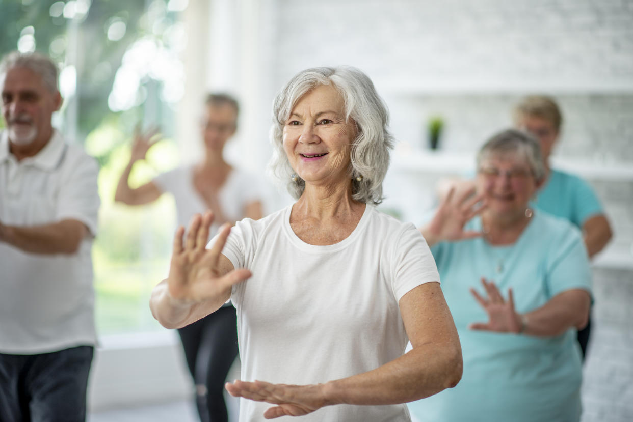 A group of seniors spend an afternoon indoors in a health center. They are doing group tai chi together.