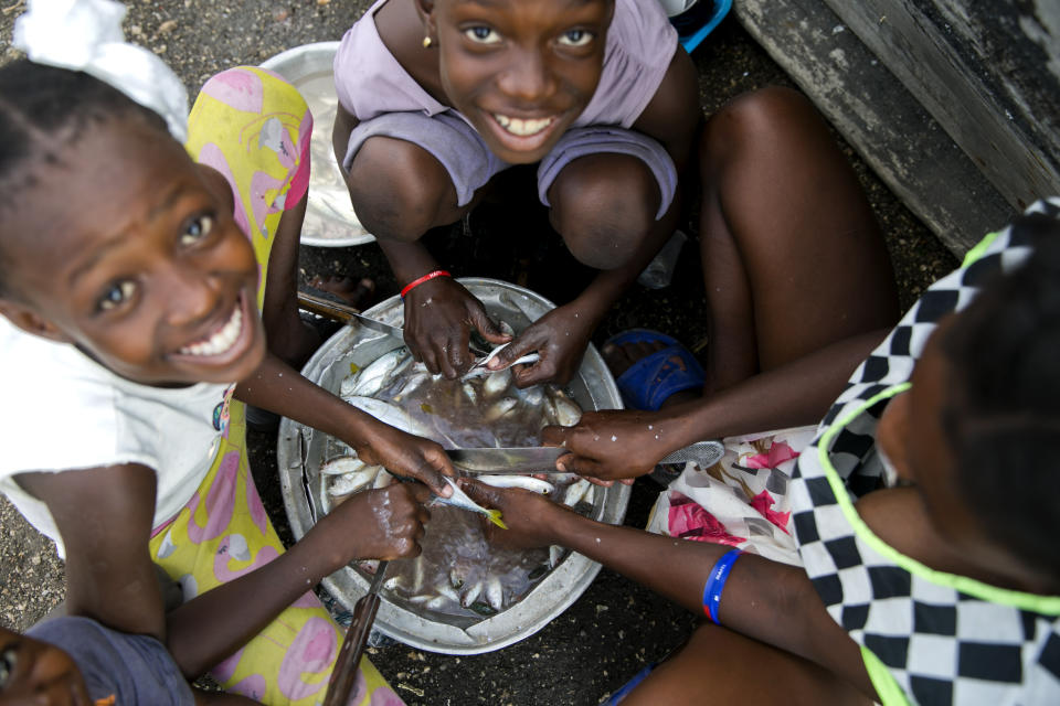 In this Dec. 3, 2019 photo, children help their mother by preparing fish to fry and sell at the Cite Soleil slum of Port-au-Prince, Haiti. A growing number of families across Haiti can't afford to buy enough food since protests began in Sept., with barricades preventing the flow of goods between the capital and the rest of the country. (AP Photo/Dieu Nalio Chery)