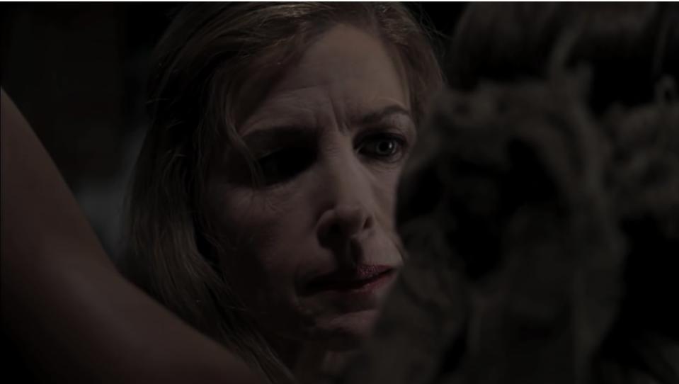 Still from the movie "The Girl Next Door" with actor Blanche Baker in the dark, looking menacingly at a woman who has been tied up