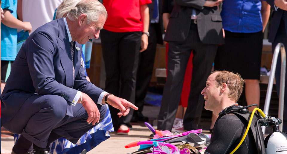 King Charles bends down to talk to his son Prince William while he is in a swimming pool wearing diving gear. 