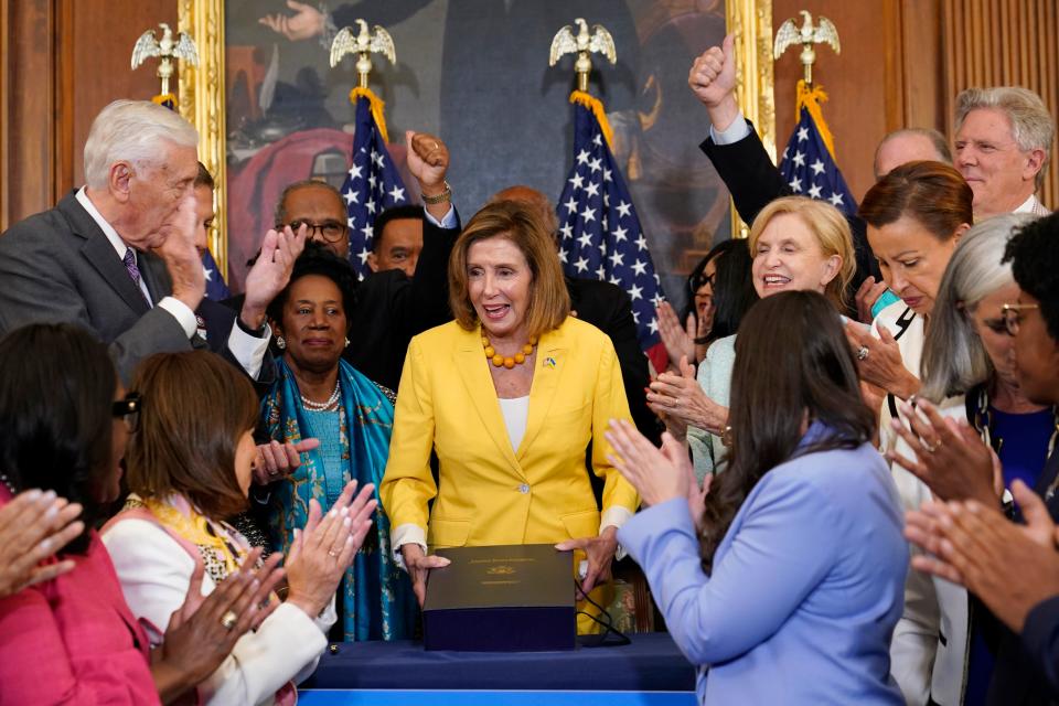 House Speaker Nancy Pelosi of Calif., surrounded by House Democrats, stands up after signing the Inflation Reduction Act of 2022 during a bill enrollment ceremony on Capitol Hill on Friday.