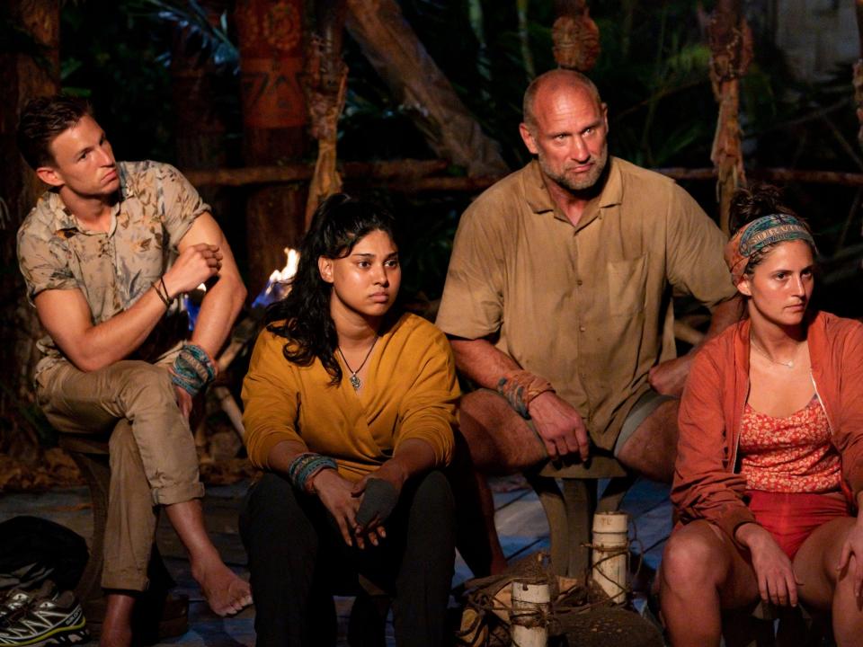 Four contestants sit near a fire at the tribal council