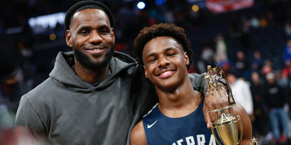 LeBron James puts his arm around his son Bronny while Bronny holds a trophy in 2019.