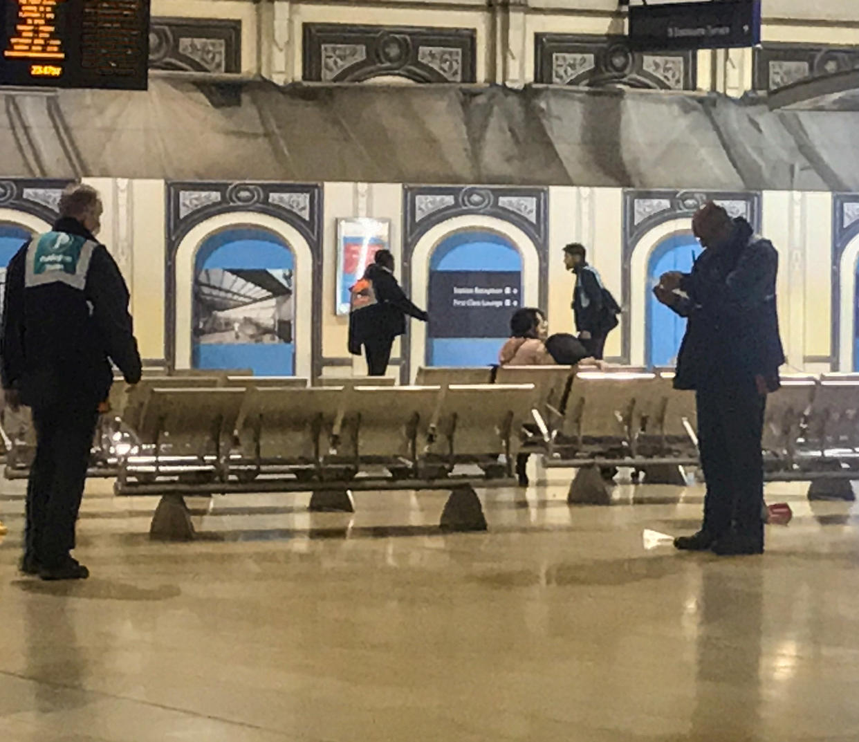 A woman sits alone on some seating at Paddington station surrounded by railway staff after the transport hub was partially cordoned off after two people fell ill with a "suspected virus outbreak". (Mack Grenfell/SWNS)