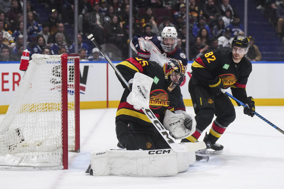 Vancouver Canucks goalie Thatcher Demko (35) makes a save as Ian Cole (82) and Columbus Blue Jackets' Boone Jenner, back left, watch during the second period of an NHL hockey game Saturday, Jan. 27, 2024, in Vancouver, British Columbia.(Darryl Dyck/The Canadian Press via AP)