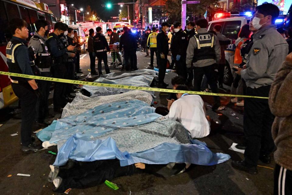 Bodies covered in sheets on a street, surrounded by emergency workers