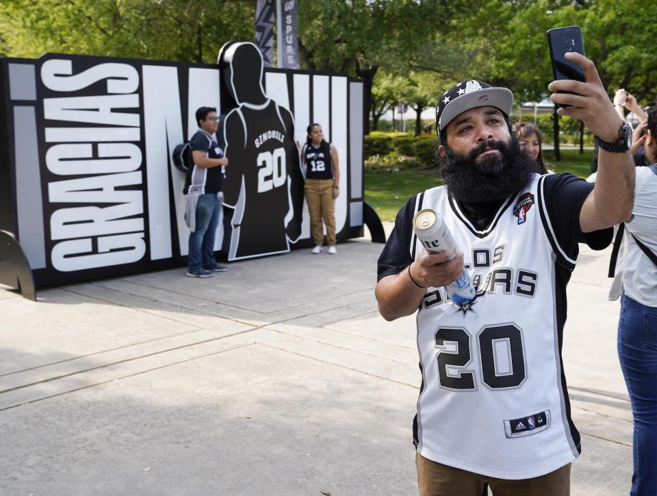 San Antonio Spurs fan Mike Belfort takes a photo in front of a sign thanking Spurs legend Manu Ginobili before an NBA basketball game against the Cleveland Cavaliers, Thursday, March 28, 2019, in San Antonio. Ginobili's jersey will be retired after the game. (AP Photo/Darren Abate)