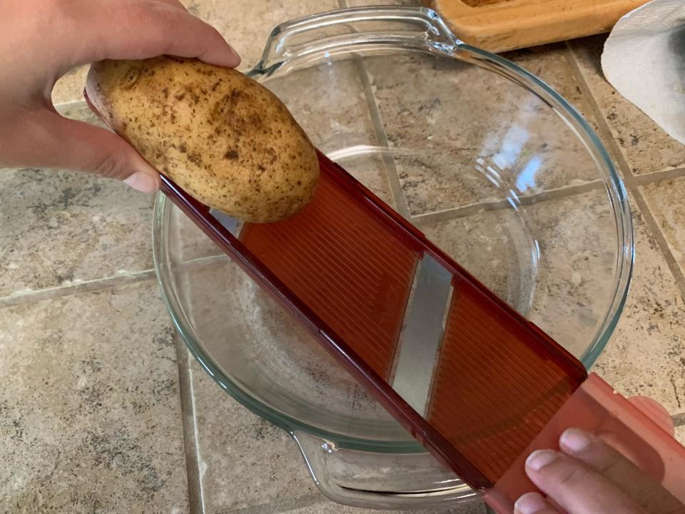 Slicing a potato using a red slicing tool over a glass bowl