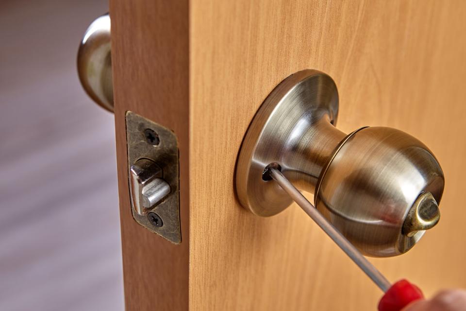 Person fixes door handle rose with screw, using a screwdriver.