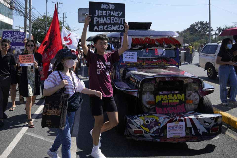 An activist holds a sign as he passes by a passenger jeepney during a transport strike in Quezon city, Philippines on Monday, March 6, 2023. Philippine transport groups launched a nationwide strike Monday to protest a government program drivers fear would phase out traditional jeepneys, which have become a cultural icon, and other aging public transport vehicles. (AP Photo/Aaron Favila)