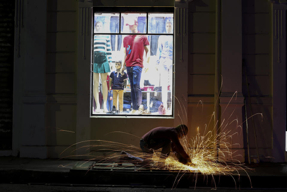 A metalworker fixes a fence of a fashion shop in downtown San Salvador, El Salvador, late Friday, March 3, 2023. Security at nighttime entertainment centers in the historic center has improved for Salvadorans during the exception regime decreed almost a year ago by the government. (AP Photo/Salvador Melendez)